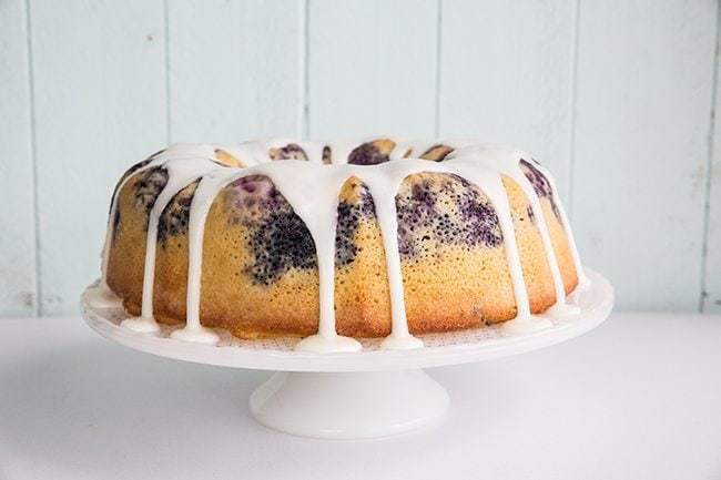 Blueberry Lime Bundt Cake on white cake holder drizzle with lime glaze