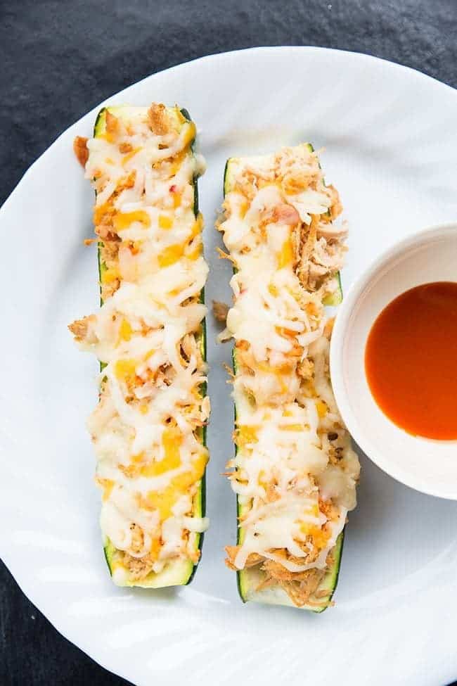 2 pieces of Cheesy Buffalo Chicken Zucchini Boats in a white plate with a cup of dipping sauce 