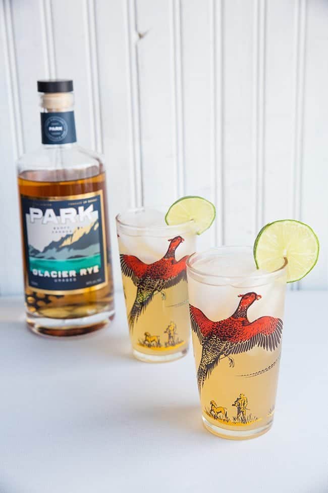 Rye Mule in sweet pheasant cocktail glasses garnish with a slice of lime. A bottle of Park brand glacier rye on background