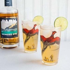 Rye Mule in sweet pheasant cocktail glasses garnish with a slice of lime. A bottle of Park brand glacier rye on background