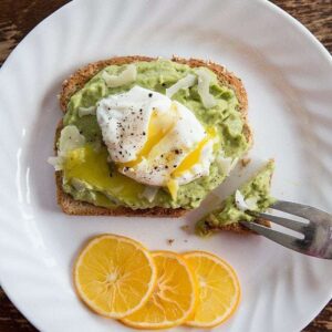 white plate with 3 lemon slices, an avocado toast and egg with Parmesan cheese