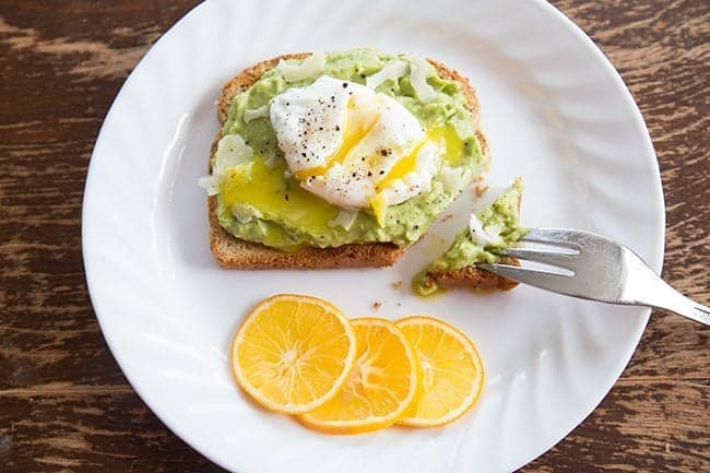 Avocado Toast in a white plate garnish with slices of Meyer lemon