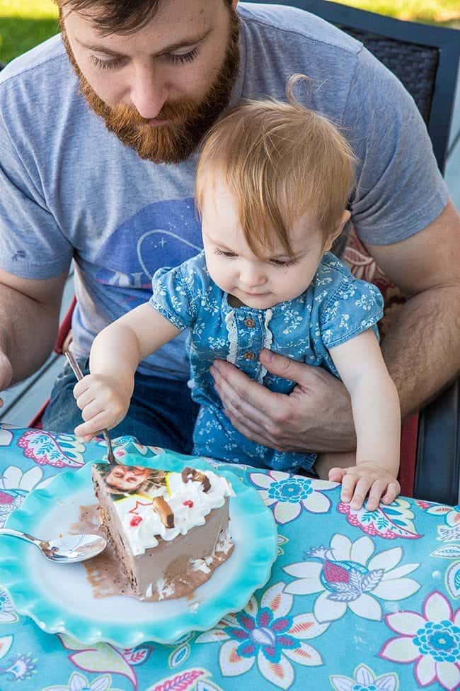 man holding his cute baby and letting her dig into that cake using a spoon