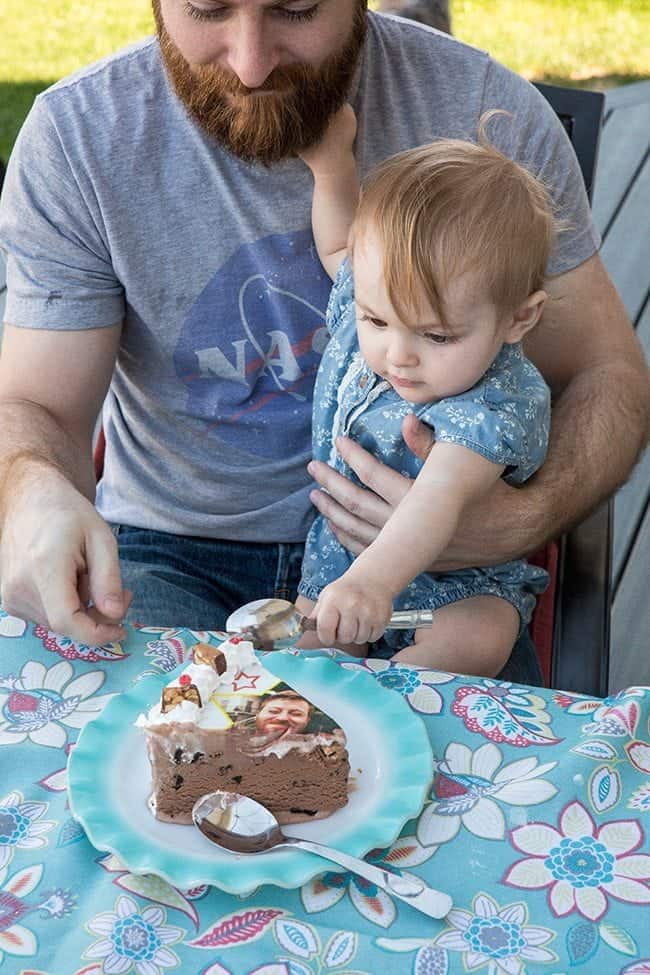 man holding his cute baby and letting her dig into that cake using a spoon