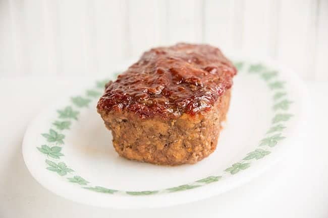 white plate with baked Meatloaf topped with sauce on white background