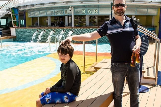 Son sitting while his Father holding 2 drinks in front of Royal Caribbean's Brilliance of the Seas Pool Bar