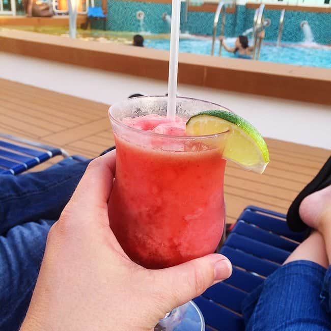 holding a glass of strawberry daiquiri with a slice of lime