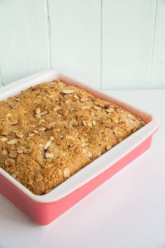 Strawberry Plum Crumble Cake with crispy almond topping in a pink baking dish