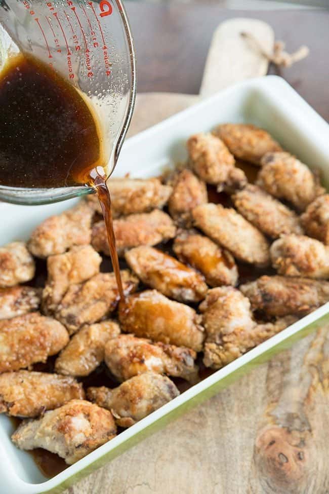 pouring sauce all over batter and fried wings