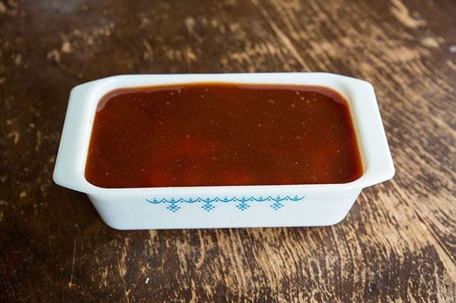 ketchup based sweet and sour sauce on top of meatloaf in a white baking pan