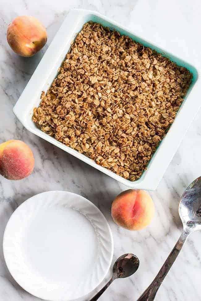 blue pan full of combined oat mixture, an empty white plate and 3 fresh peaches around