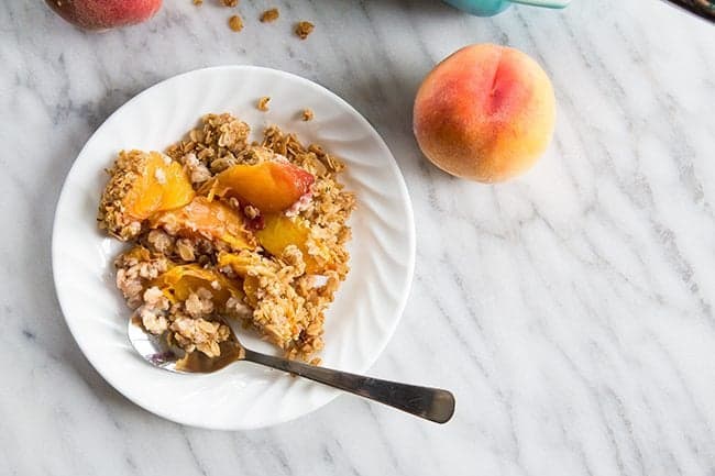 Peach Crisp in a white plate with spoon, peach fruit on a marble background