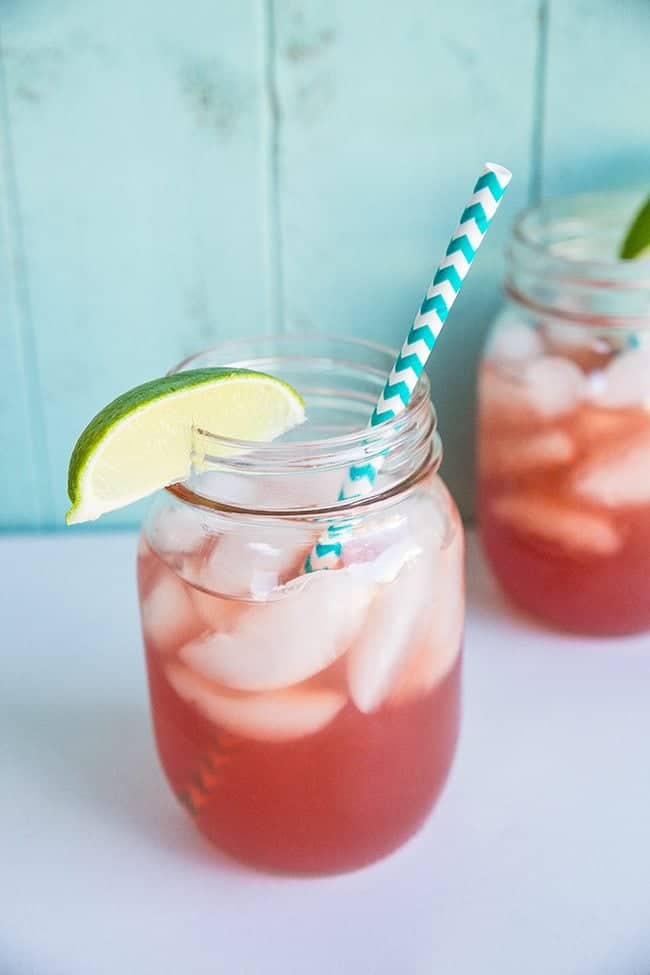 close up Sea Breeze Cocktail in a large mason glass jar topped with ice and garnished with a lime wedge