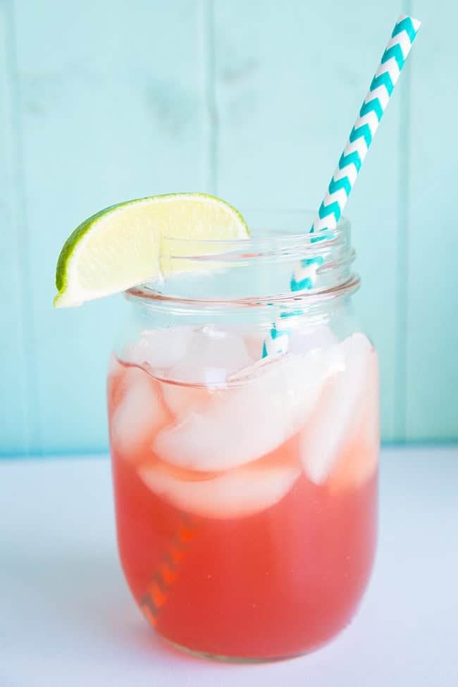 close up Sea Breeze Cocktail topped with ice, garnished with a lime wedge and a paper straw