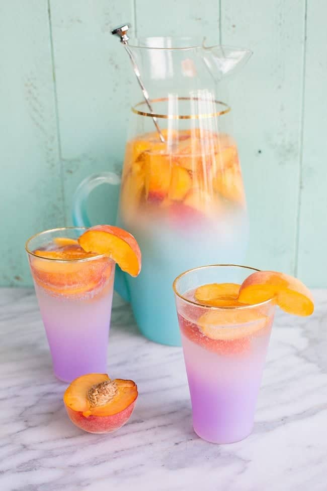 Pitcher and glasses of Sparkling Peach Sangria garnish with a slice of fresh Peach