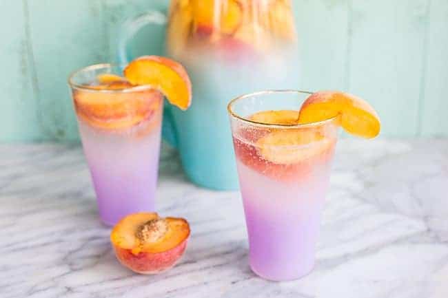 Pitcher and glasses of Sparkling Peach Sangria garnish with a slice of fresh Peach