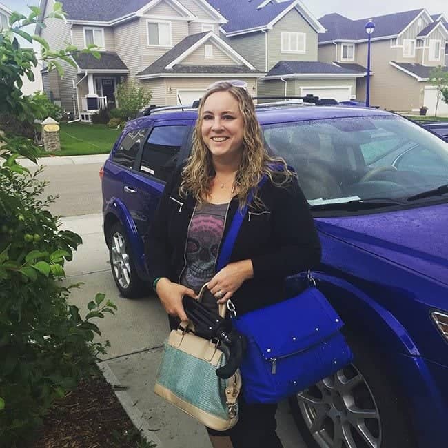 woman standing beside a blue car holding her bags and black umbrella