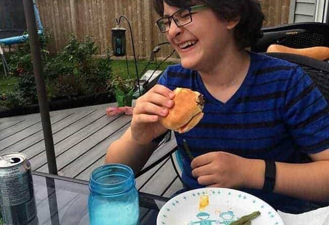 young boy in eye glasses laughing while sitting and holding a burger