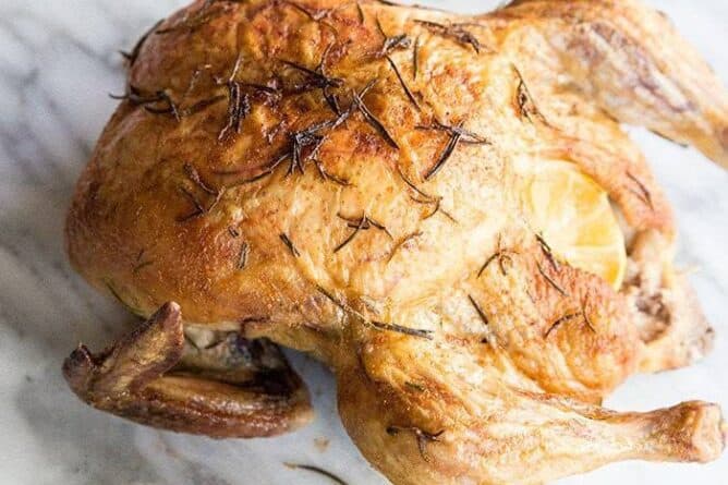Whole Roasted Chicken with Lemon and Rosemary on a marble background