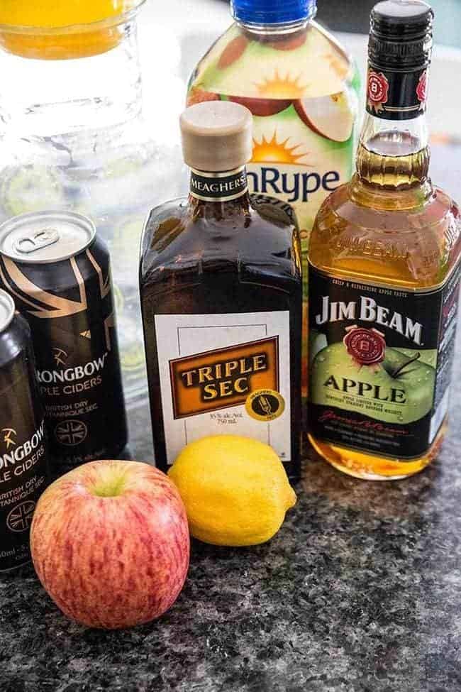 bottle of apple Bourbon and triple sec together with cans of hard apple cider, fresh apple and lemon