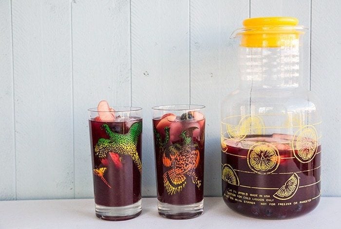 a large pitcher with a lid and 2 vintage glasses with Red Wine Sangria on white background