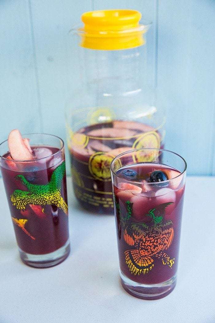 close up of 2 vintage glasses with Red Wine Sangria and a large pitcher with lid at the back