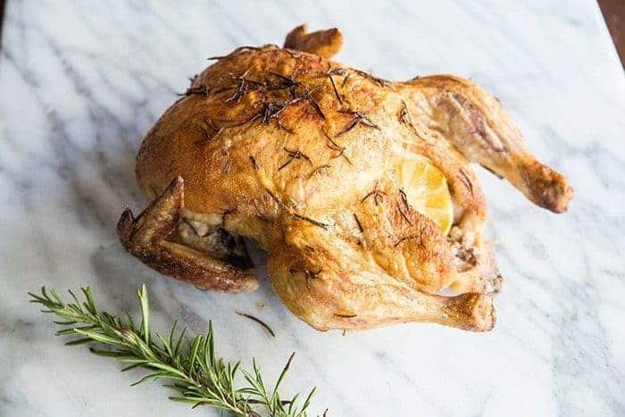 Whole Roasted Chicken with Lemon and Rosemary on a marble table