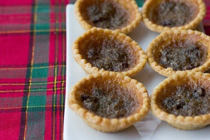 red Christmas tablecloth underneath a plate with 6 pieces of Butter Tarts