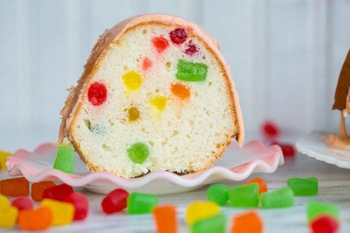 a slice of Gumdrop Cake in a white dessert plate, some pieces of gumdrops on the table