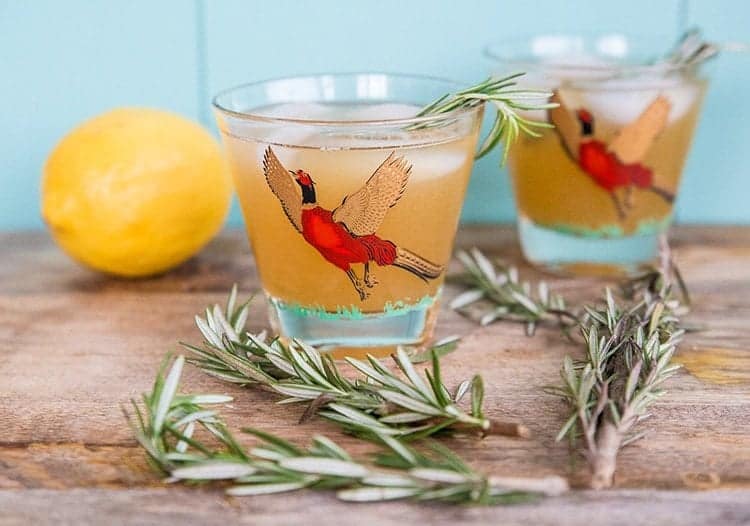 Maple Rosemary Bourbon Sour in a pheasant cocktail glasses, springs of rosemary and fresh lemon on background