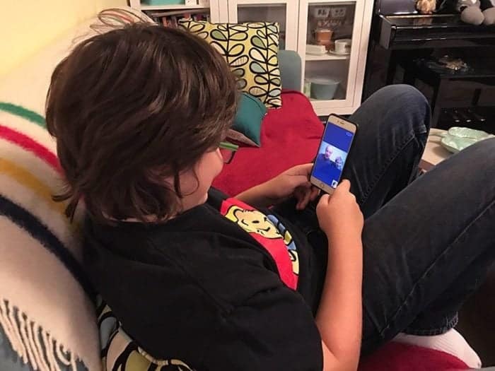 young boy sitting in the couch watching from his mobile phone