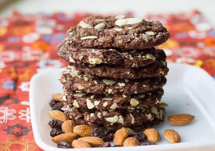 a stack of Old Fashioned Chewy Chocolate Raisin Cookies in a white plate with almonds and raisins