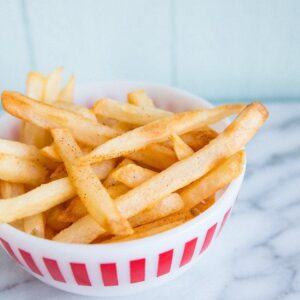 Homemade fries in a small bowl on marble nackground
