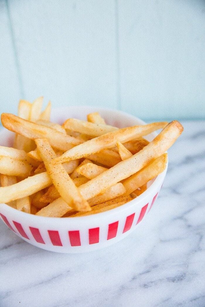 Homemade fries in a small bowl on marble nackground