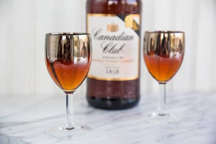 Two glasses of Classic Manhattan cocktails with a bottle of Canadian club whiskey on background