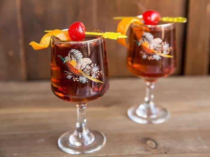 Manhattan cocktail drink in vintage pheasant glasses topped with maraschino cherry