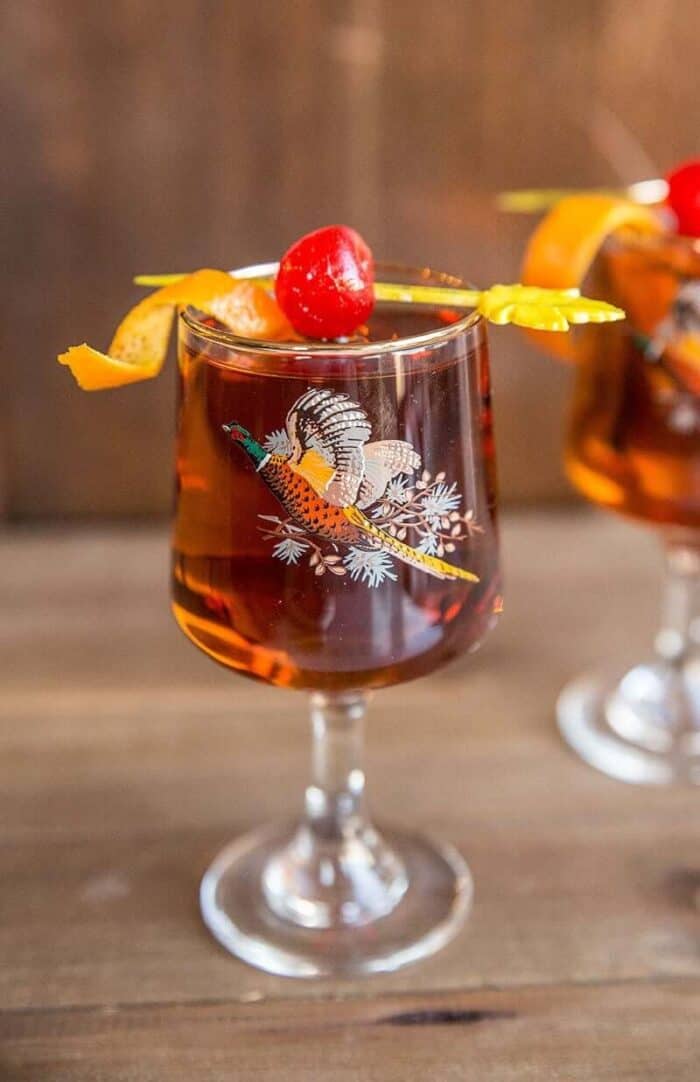 Manhattan cocktail drink in vintage pheasant glasses with cherry and orange garnish