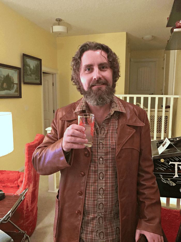 A man with beard, wearing leather jacket, holding his drink