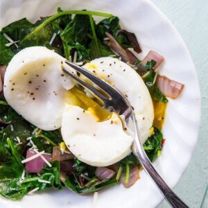 slicing the poached egg on top of Mixed Greens & Cajun Onions Vegetable Breakfast Goal Bowl