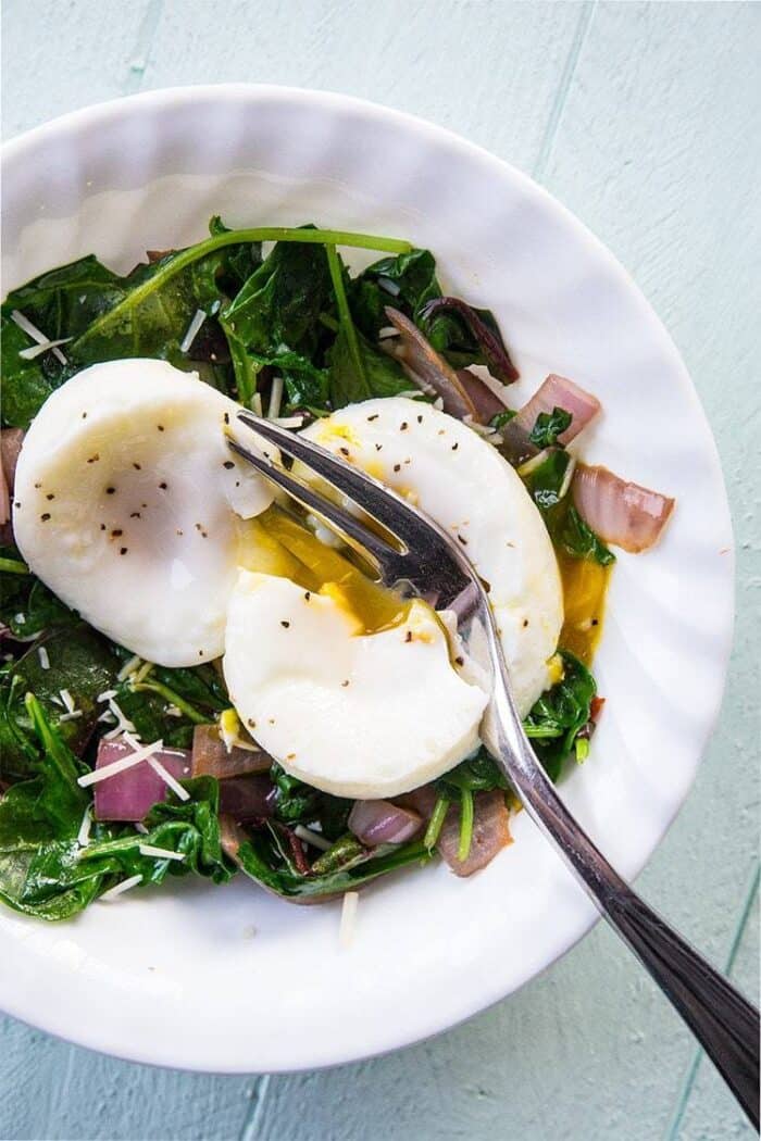 white plate with vegetables and bacon strips topped with poached eggs