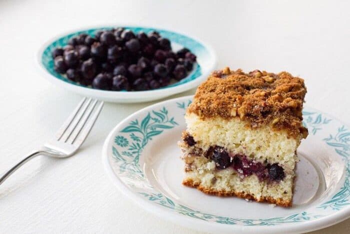 A Slice of Saskatoon Coffee Cake in a small white plate and blueberries in another small plate on the side