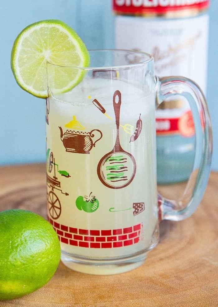 close up of Classic Moscow Mule Recipe in a Vintage Hazel Atlas Glass, garnish with a slice of lime and a bottle of vodka on background