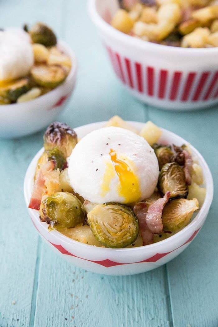 A bowl with roasted brussels sprouts, white sweet potato & bacon topped with poached egg