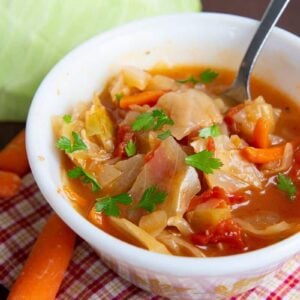 Checkered red kitchen cloth underneath cabbage soup in a bowl garnish with parsley leaves