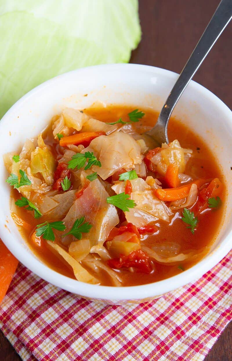 Checkered red kitchen cloth underneath cabbage soup in a bowl garnish with parsley leaves