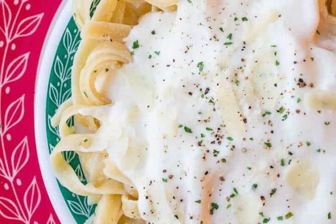 Close up of Alfredo Sauce on fettuccine noodles on red and green Pyrex plates