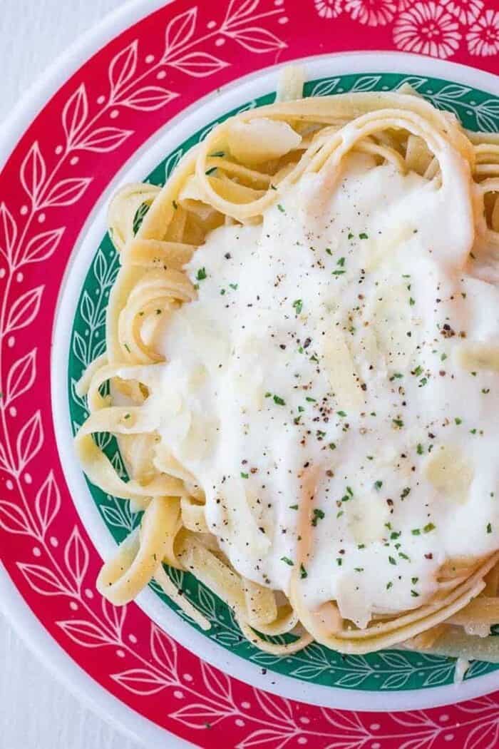 Close up of Alfredo Sauce on fettuccine noodles on red and green Pyrex plates 