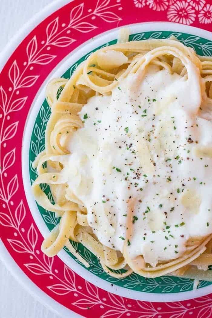 Close up of Alfredo Sauce on fettuccine noodles on red and green Pyrex plates