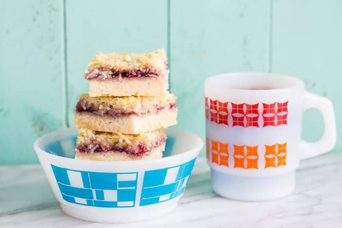 Stack of Coconut Grape Jam Bars in a Close up Stack of Coconut Grape Jam Bars in a White bow printed with blue and a white mug beside it