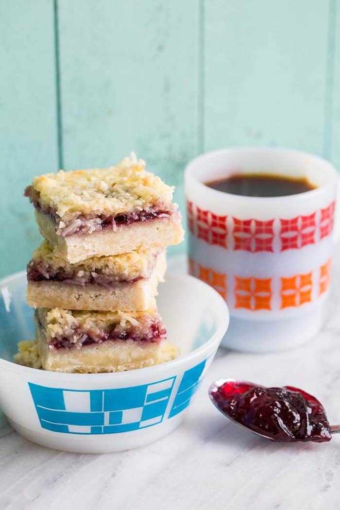 Stack of Coconut Grape Jam Bars in a Close up Stack of Coconut Grape Jam Bars in a White bow printed with blue, a white mug beside it and a spoonful of Coconut Grape Jam